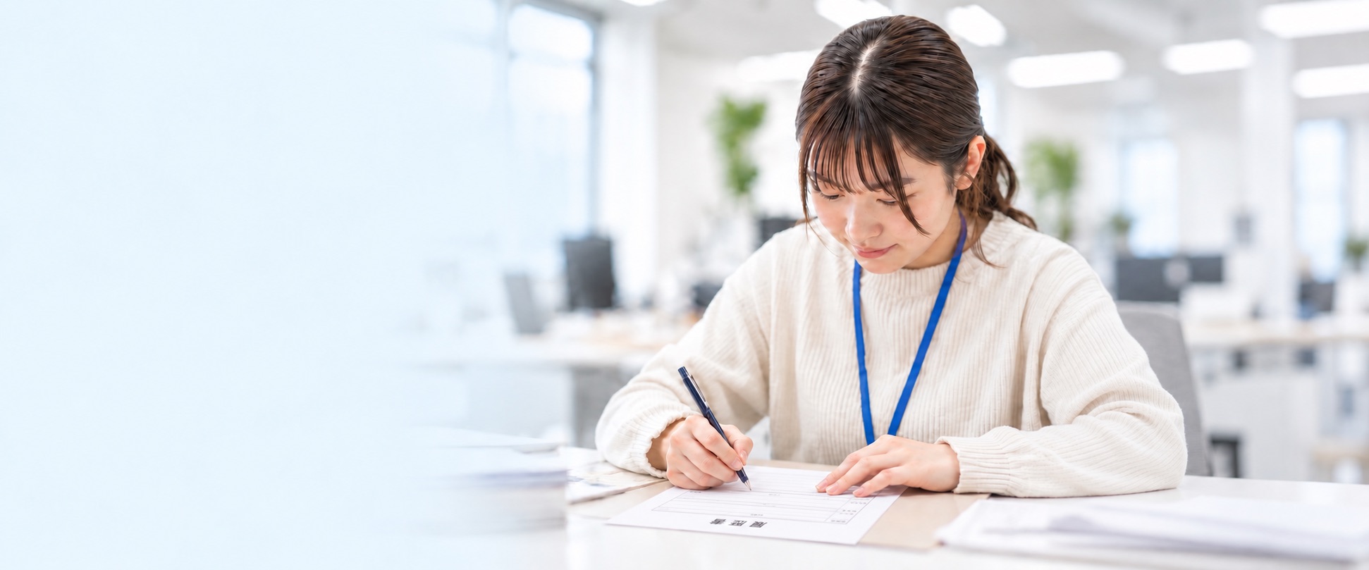明るいオフィスでペンを持ち、書類に記入する女性のイメージ写真